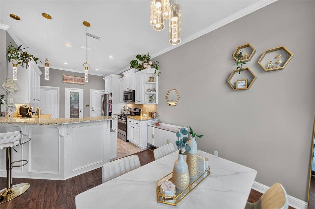 Kitchen featuring white cabinetry, stone-surface countertops, decorative pendant lighting, stainless steel appliances, and wood-finish flooring