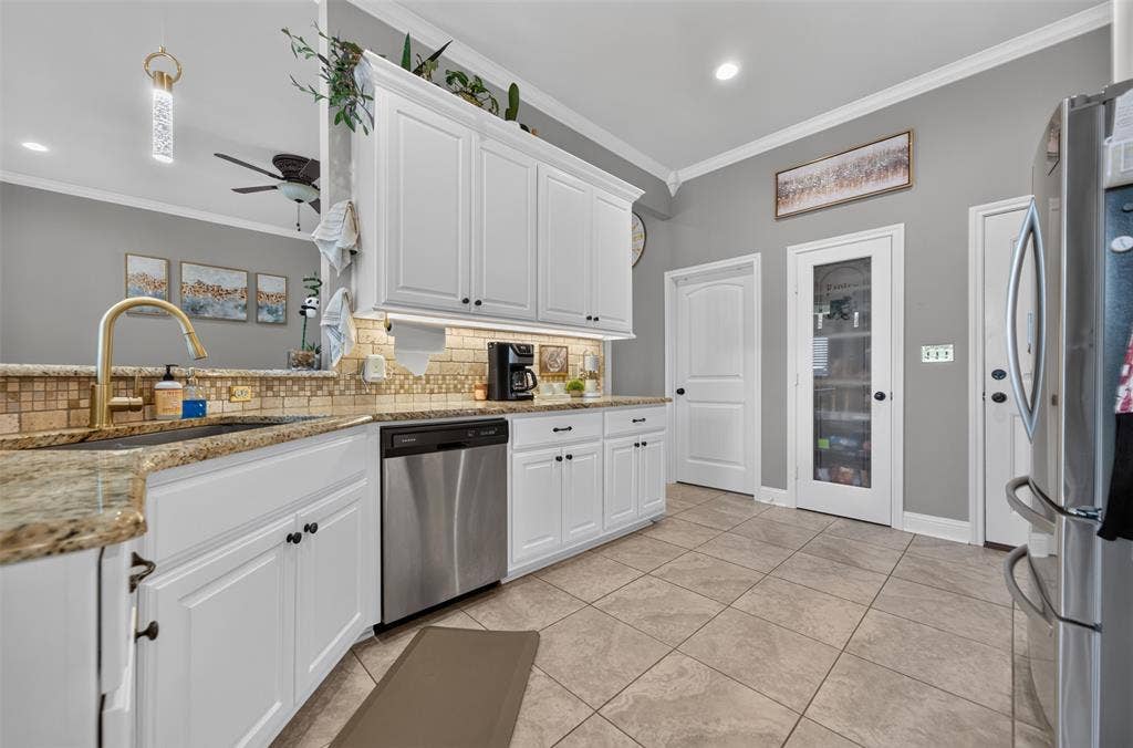 Kitchen featuring white cabinetry with crown molding, stone-patterned countertops, a decorative tile backsplash, stainless steel appliances, and a glass-panel pantry door