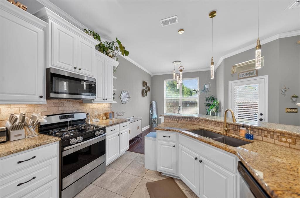 Kitchen featuring white cabinetry, stone-finish countertops, brick-pattern backsplash, stainless steel appliances, and pendant lighting