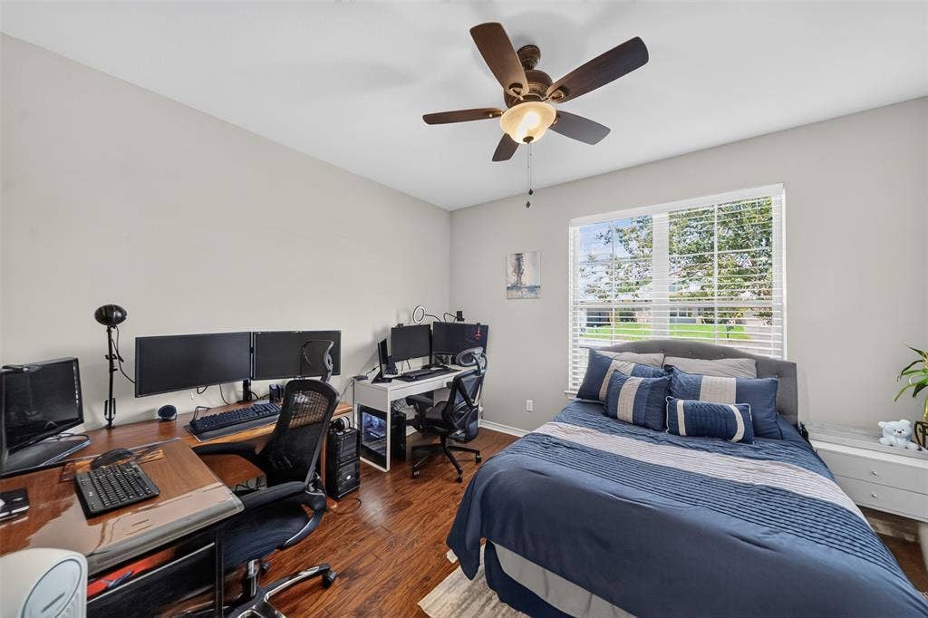 Neutral-toned interior room featuring wood-finish flooring, a multi-blade ceiling fan with an integrated light fixture, and a large window with horizontal blinds