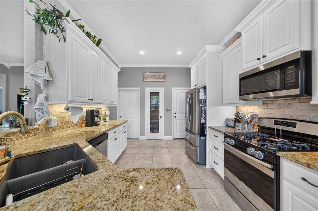 Kitchen featuring white shaker-style cabinetry, stone countertops, stainless steel appliances, a tile backsplash, and ceramic tile flooring