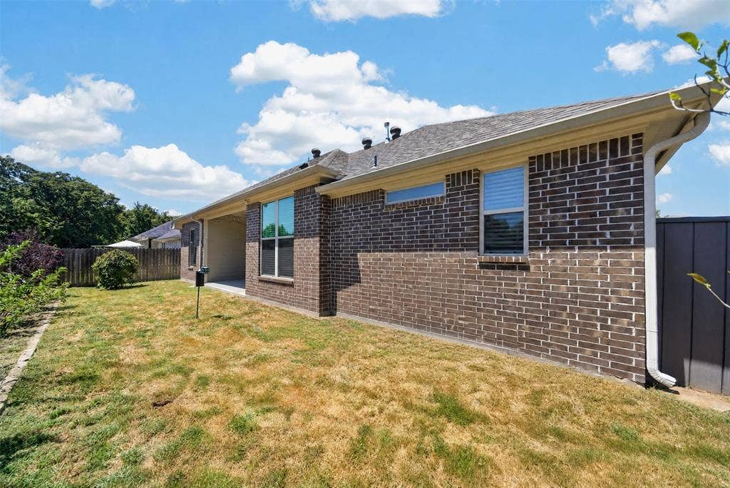 Brick exterior featuring a covered patio, shingle roof, and wooden privacy fencing
