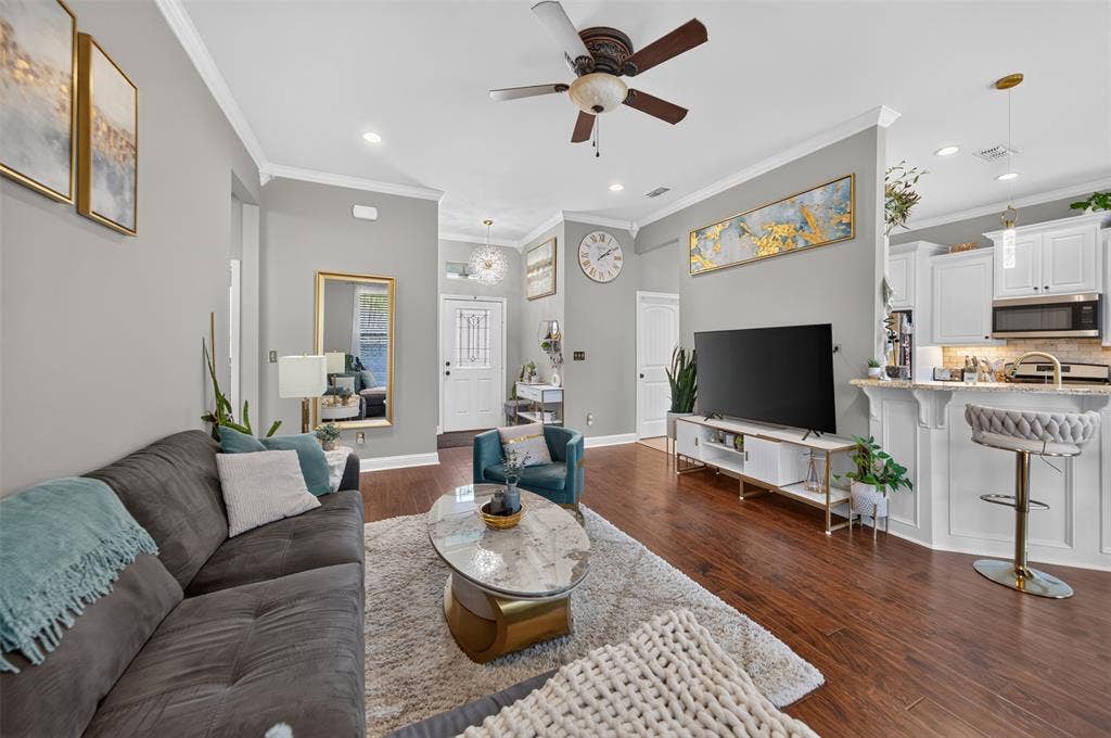 Living area featuring wood-finish flooring, crown molding, recessed lighting, ceiling fan, and a breakfast bar with stone-finish countertops