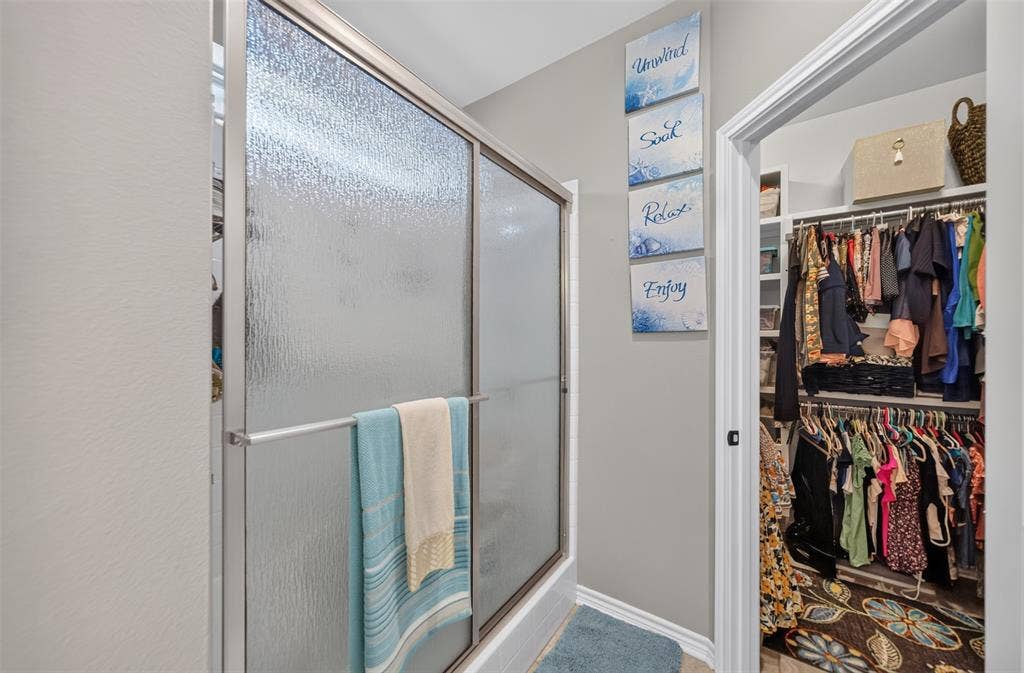 Shower enclosure featuring textured privacy glass and a metal frame, accompanied by a walk-in closet with built-in shelving and hanging rods