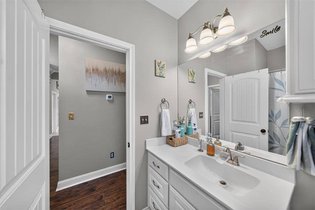 Bathroom vanity featuring a white countertop with an integrated basin, white cabinetry with metallic hardware, a full-width wall mirror, and a three-light fixture
