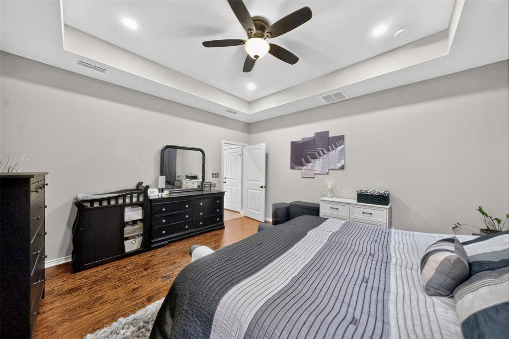 Tray ceiling with recessed lighting and a central ceiling fan, paired with wood-finish flooring and arch-top interior doors