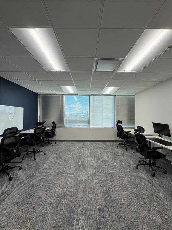Office space featuring a dropped acoustic ceiling, integrated fluorescent lighting panels, wall-to-wall carpeting, and a built-in dry erase board