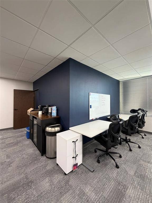 Neutral-toned carpeted flooring, drop ceiling with recessed lighting, accent wall, and horizontal window blinds