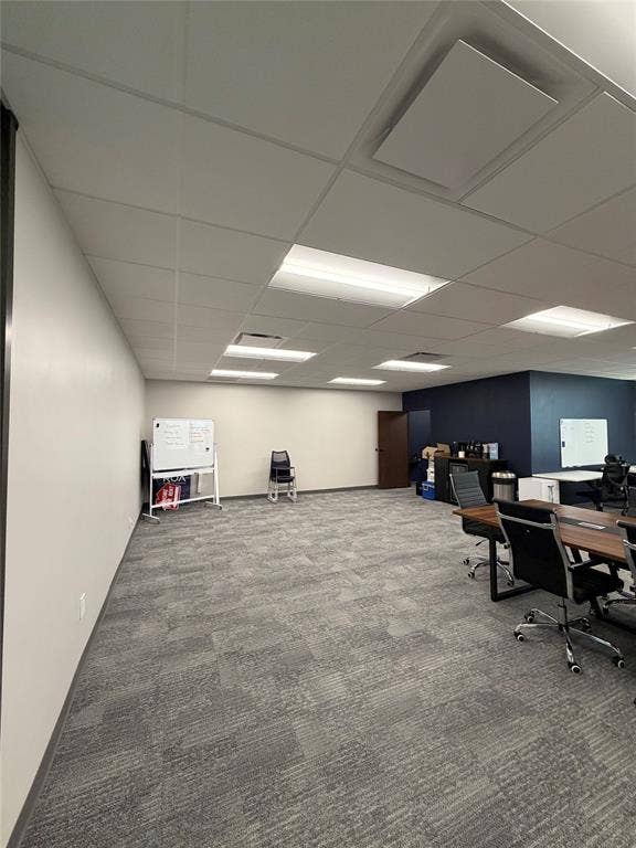Open workspace featuring a drop ceiling with recessed fluorescent lighting, neutral-toned carpet tiles, and contrasting dark-toned accent walls