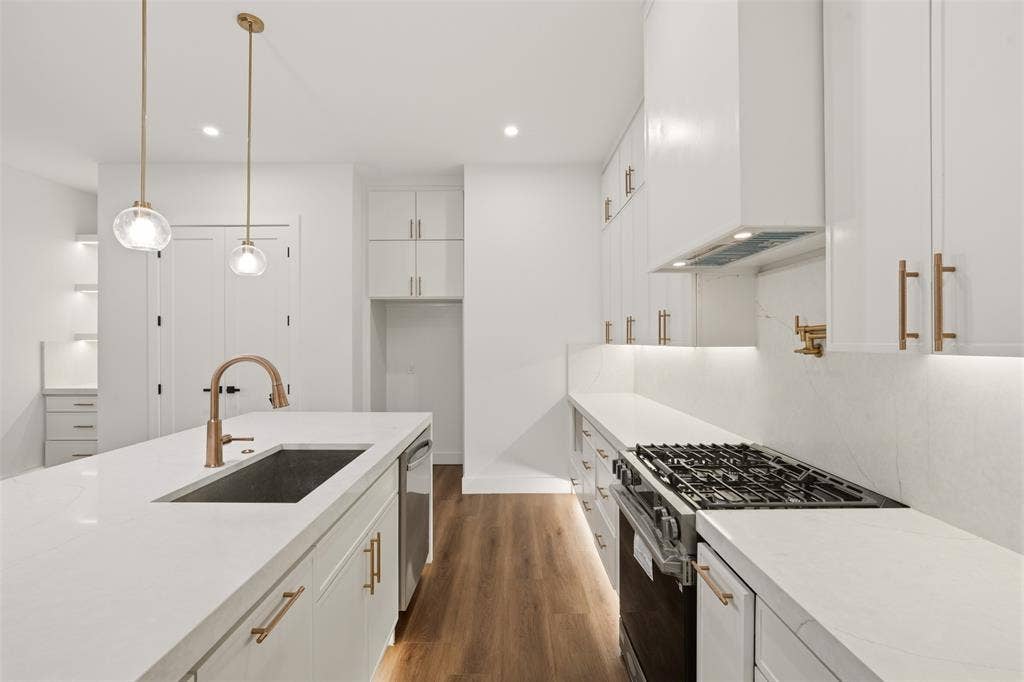 Kitchen featuring white shaker cabinetry, quartz countertops, a stainless steel gas range with a matching range hood, gold-tone hardware, and wood-finish flooring