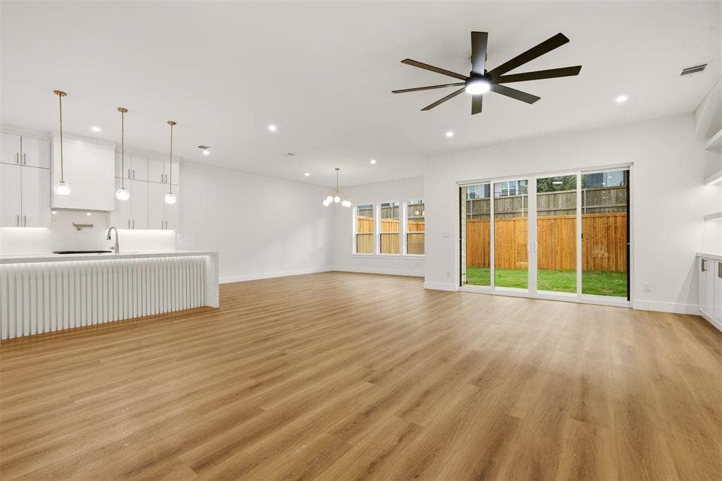 Open-concept interior featuring wood-finish flooring, a kitchen island with fluted detailing, glass sliding doors, recessed lighting, and a multi-blade ceiling fan
