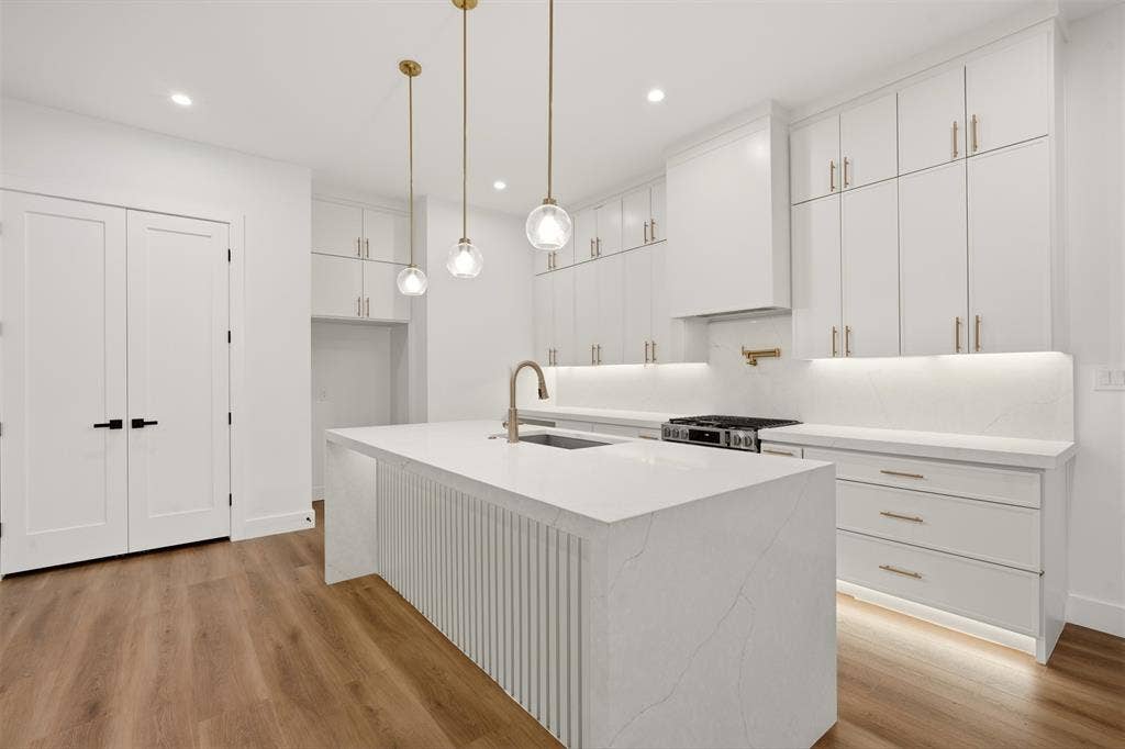 Kitchen featuring floor-to-ceiling cabinetry, a center island with waterfall edge and fluted detailing, quartz countertops, under-cabinet lighting, and wood-finish flooring
