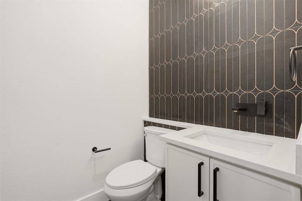 Modern vanity featuring a white countertop, under-mount sink, and matte black hardware, accented by geometric patterned wall tile and a wall-mounted faucet