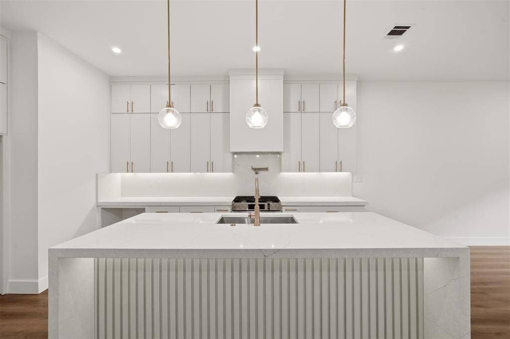 Kitchen featuring custom white cabinetry, a center island with waterfall-edge countertop and ribbed detailing, three glass pendant lights, and a stainless steel pot filler