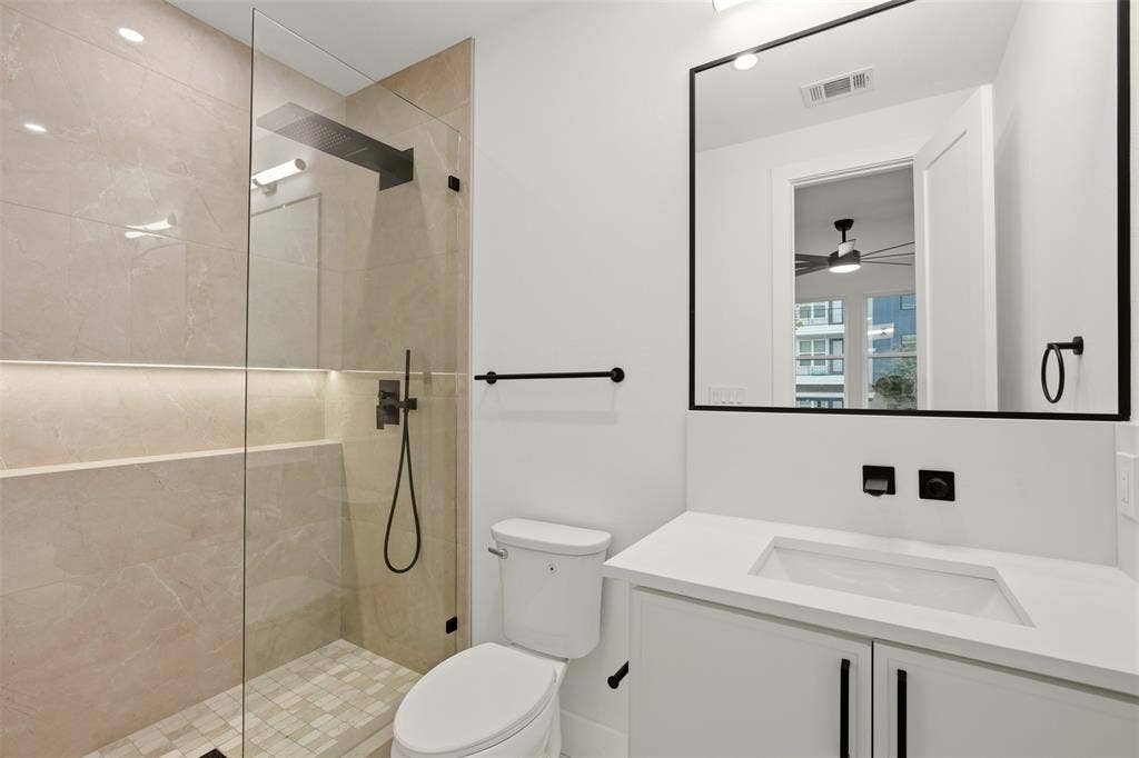 Walk-in shower with floor-to-ceiling tile, frameless glass enclosure, recessed wall niche, matte black rainfall showerhead, and floating vanity with an integrated sink and quartz countertop