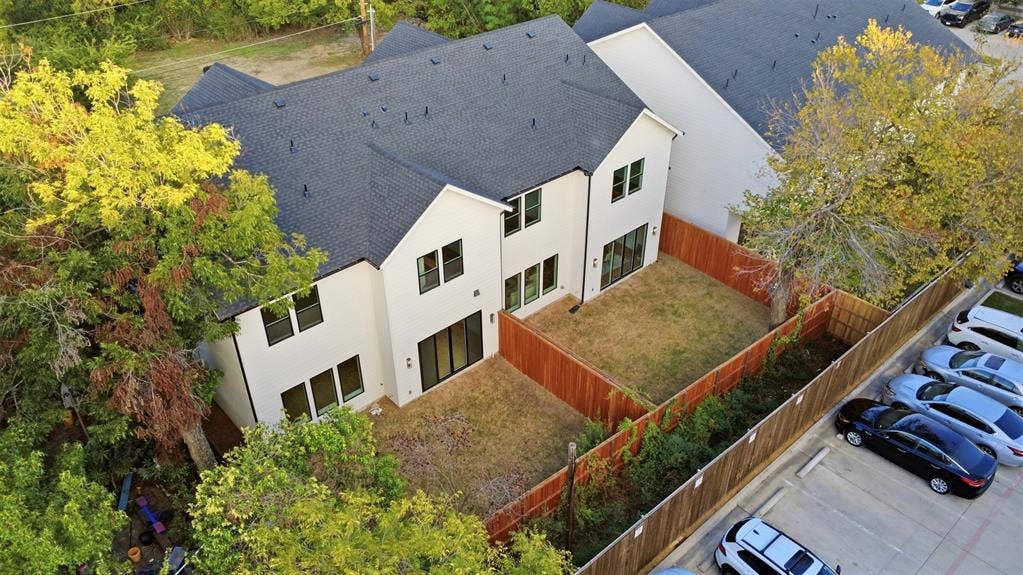 Two-story structure featuring light-colored exterior finish, a pitched asphalt shingle roof, multi-pane windows, and a wood-slat privacy fence enclosing the grounds
