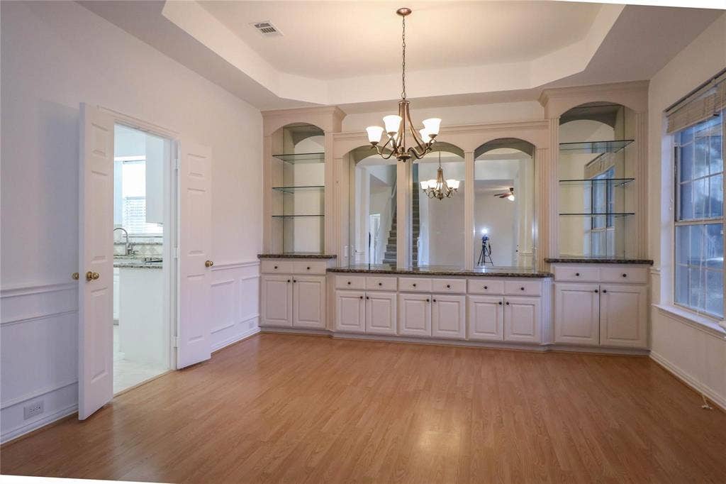 504 Renfro Court, Irving, TX 75063 Tray ceiling featuring a decorative chandelier, expansive built-in cabinetry with glass shelving, mirrored accents, and wood-finish flooring
