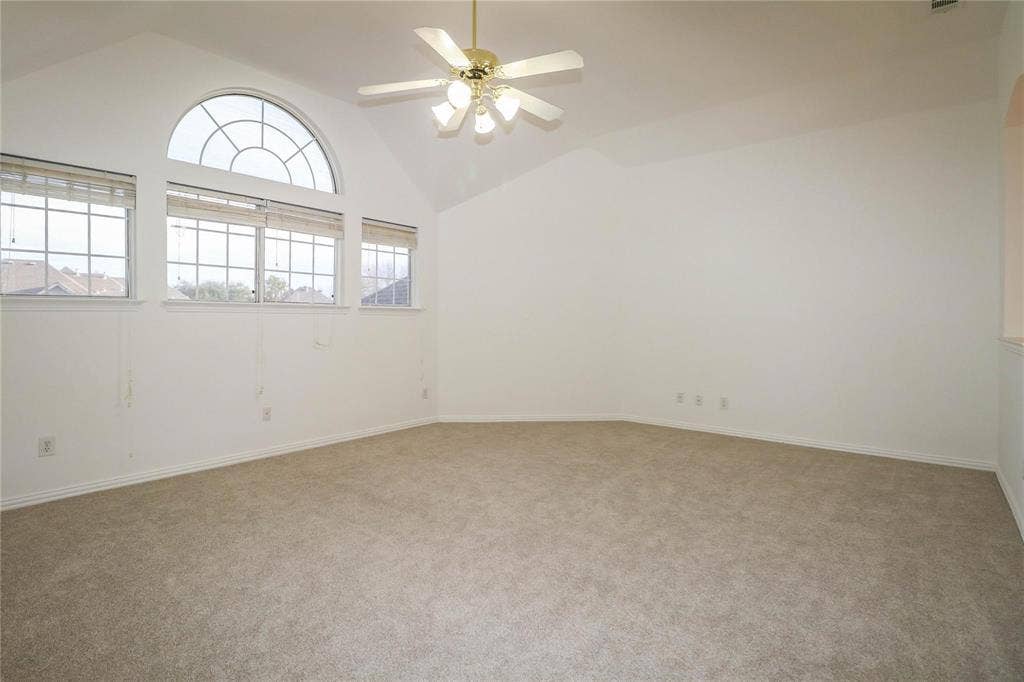 504 Renfro Court, Irving, TX 75063 Vaulted ceiling featuring a central multi-light fan, expansive wall of grid-style windows with an arched transom, and neutral carpeting