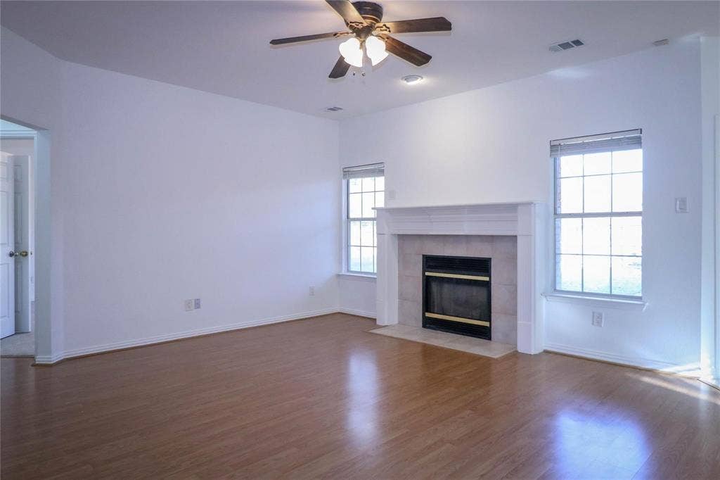 504 Renfro Court, Irving, TX 75063 Living area featuring wood-finish flooring, a fireplace with a white mantel and light-toned surround, two windows, and a ceiling fan with integrated lighting