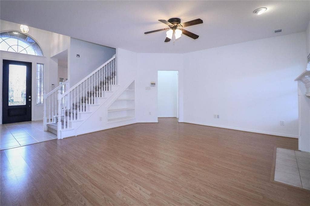 504 Renfro Court, Irving, TX 75063 Open living area featuring wood-finish flooring, a ceiling fan with integrated lighting, an arched transom window, a staircase with white balusters, and built-in under-stair shelving