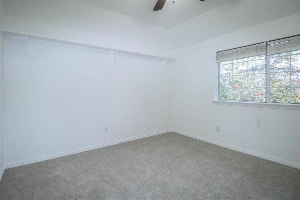 504 Renfro Court, Irving, TX 75063 Neutral-toned wall-to-wall carpeting, high ceilings, large window with horizontal blinds, ceiling fan, and built-in wall shelving
