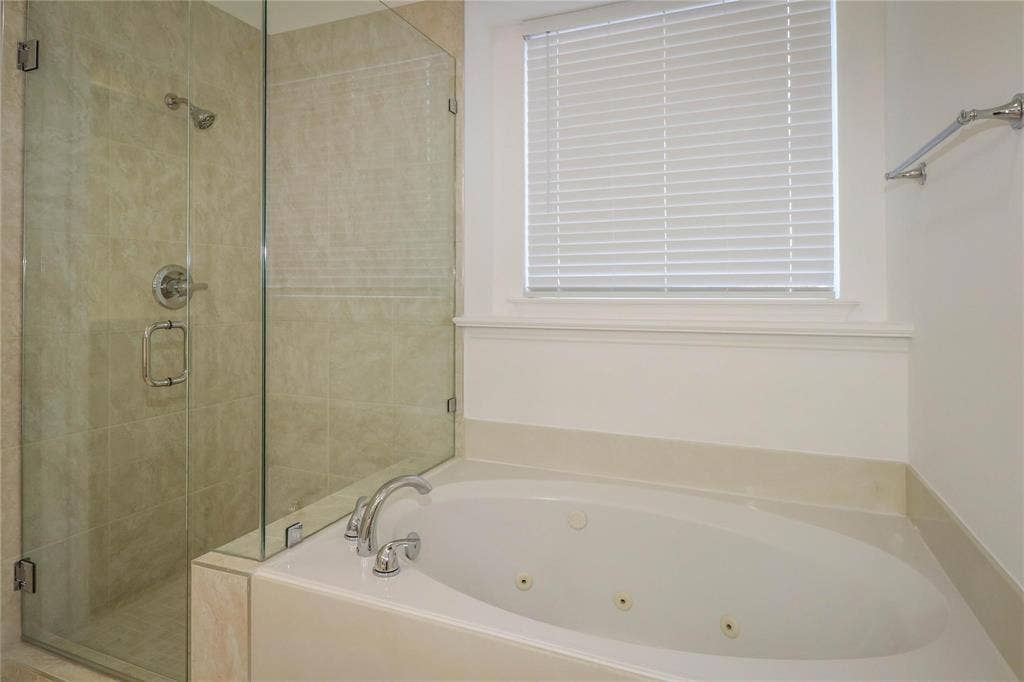 504 Renfro Court, Irving, TX 75063 Oval jetted soaking tub with a deck-mounted chrome faucet, separate walk-in shower featuring glass enclosure walls and neutral-toned tile surround, and a recessed window with fitted blinds