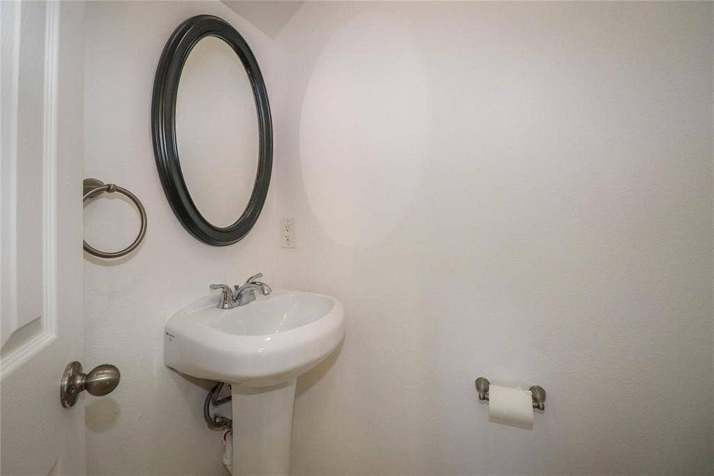 504 Renfro Court, Irving, TX 75063 Wall-mounted oval mirror with a dark frame, white pedestal sink, dual-handle chrome faucet, and circular metal towel ring