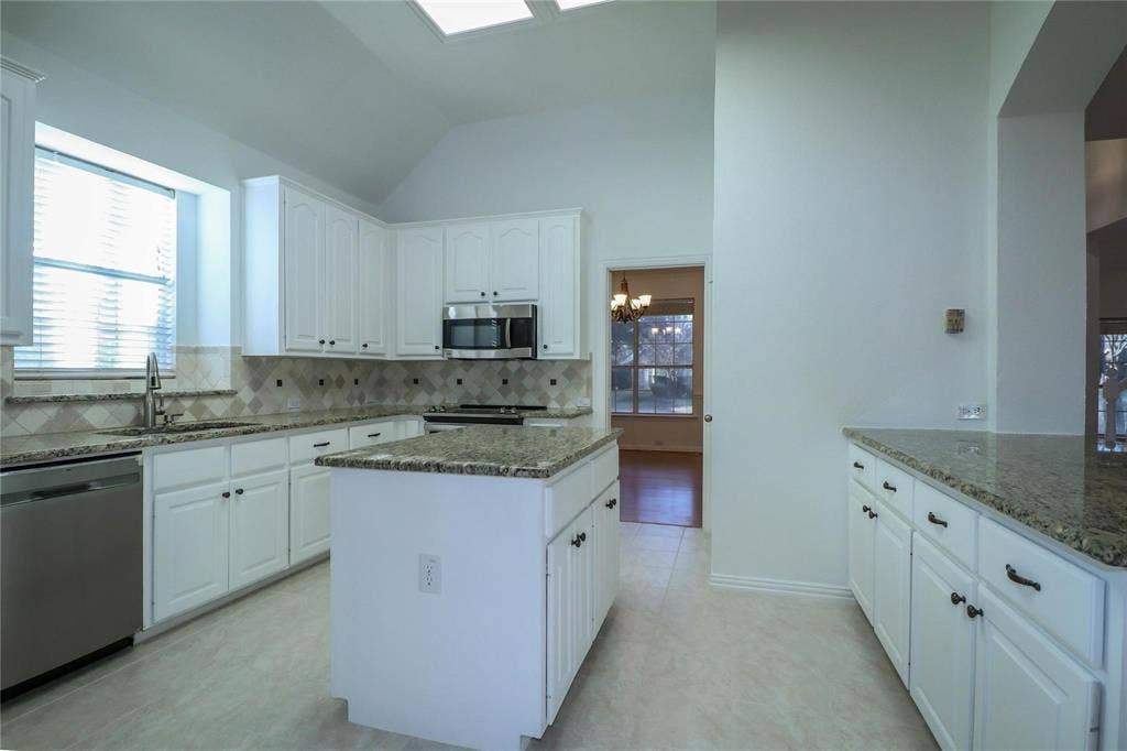 504 Renfro Court, Irving, TX 75063 Kitchen featuring white cabinetry, stone-surface countertops, center island, tiled backsplash, and vaulted ceiling with skylights