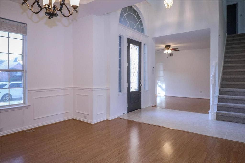 504 Renfro Court, Irving, TX 75063 Foyer featuring a high ceiling, wainscoting, wood-finish flooring, a decorative arched transom window, and a staircase with a white balustrade