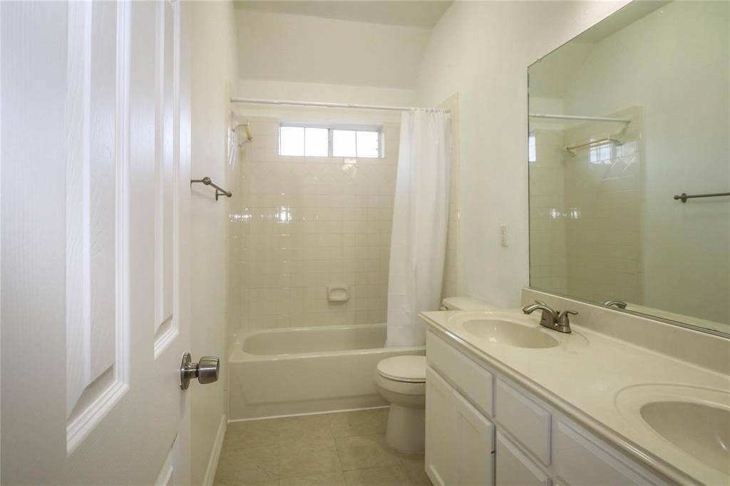 504 Renfro Court, Irving, TX 75063 Bathroom featuring a dual-sink vanity with solid-surface countertops, a porcelain tub-and-shower combination with tile surround, and a large wall-mounted mirror