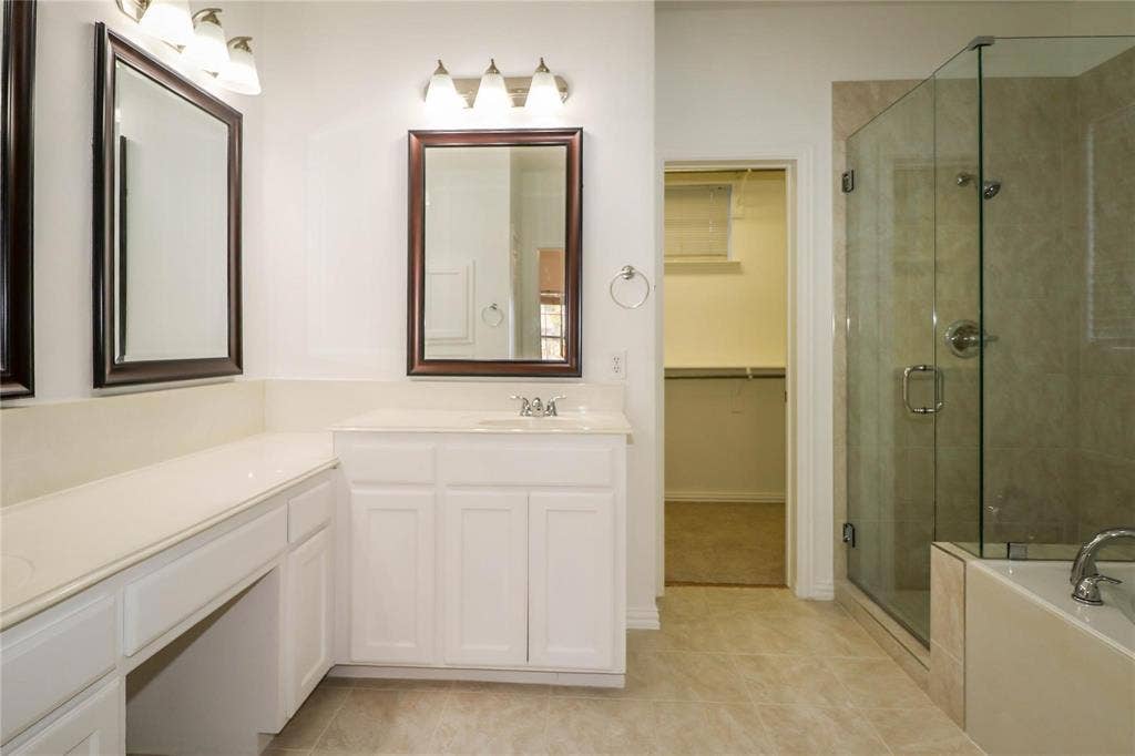 504 Renfro Court, Irving, TX 75063 White cabinetry vanity with stone countertop, framed wall mirrors, three-light fixtures, glass-enclosed shower, and built-in closet shelving