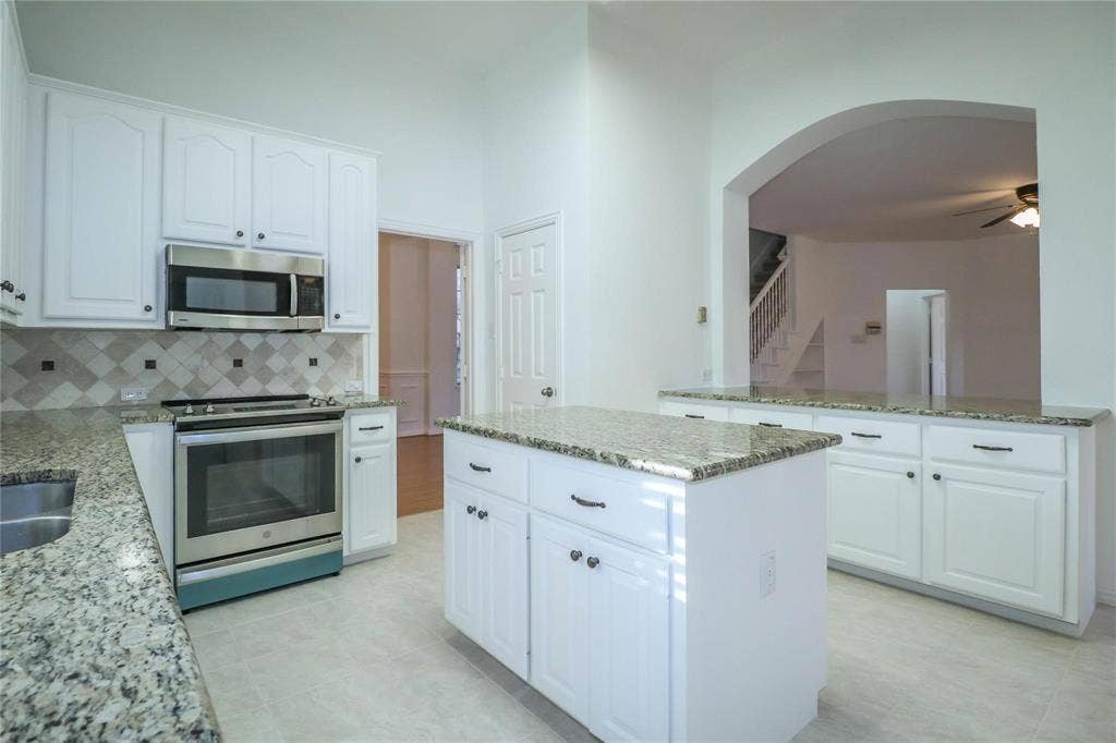 504 Renfro Court, Irving, TX 75063 Kitchen featuring white cabinetry, stone countertops, a center island, stainless steel appliances, and a tiled backsplash