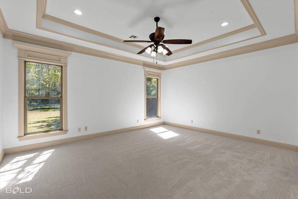 718 Duckwater Landing, Bossier City, LA 71111 Tray ceiling with crown molding, neutral carpeting, recessed lighting, ceiling fan with light fixture, and windows with decorative casing