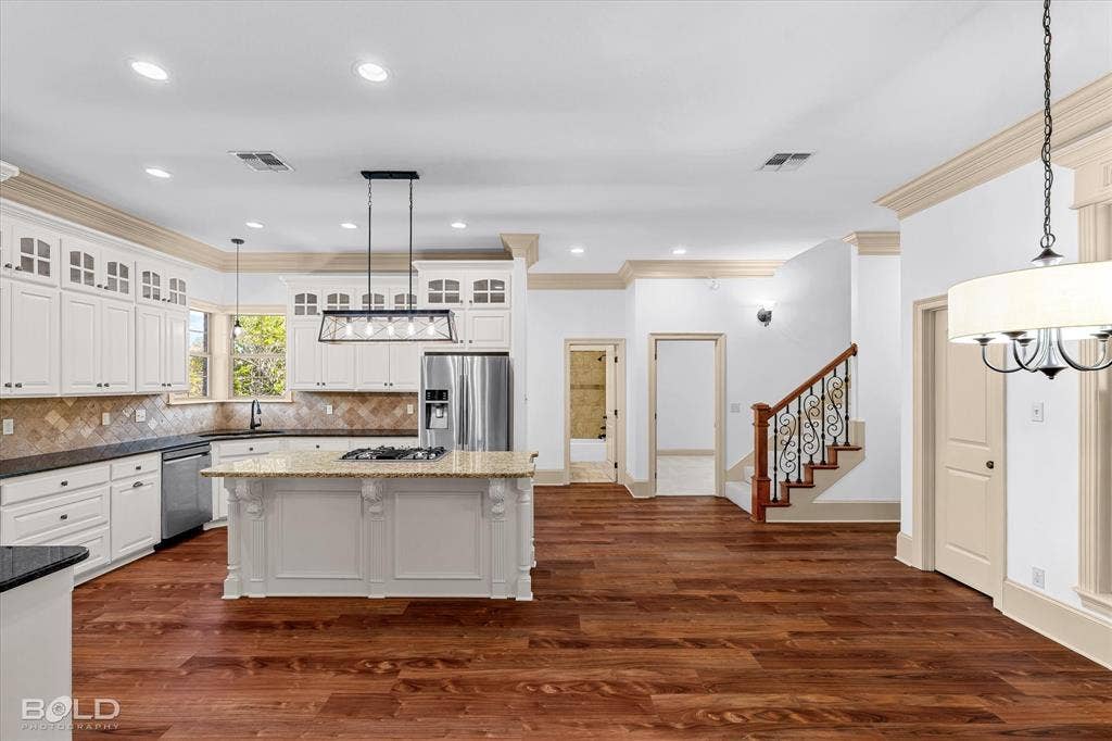 718 Duckwater Landing, Bossier City, LA 71111 Kitchen featuring white cabinetry, stone-surfaced center island with a built-in cooktop, wood-finish flooring, crown molding, and staircase with decorative wrought-iron balusters