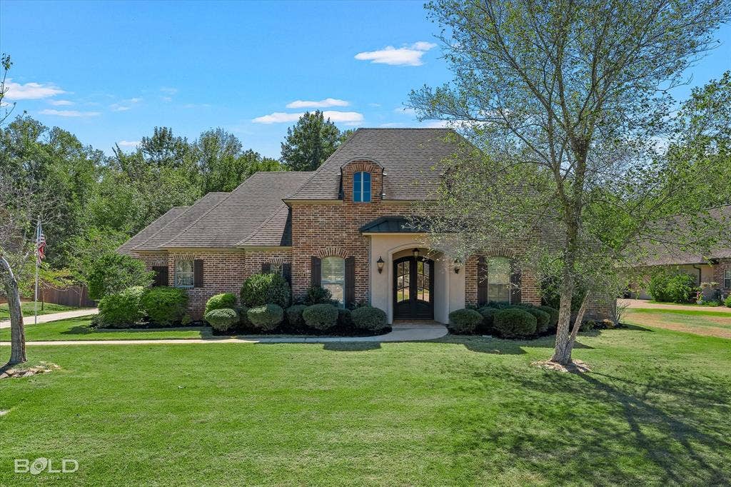 718 Duckwater Landing, Bossier City, LA 71111 Brick exterior featuring a multi-gabled roofline, an arched entryway with metal roofing detail, arched windows, and mature landscaping