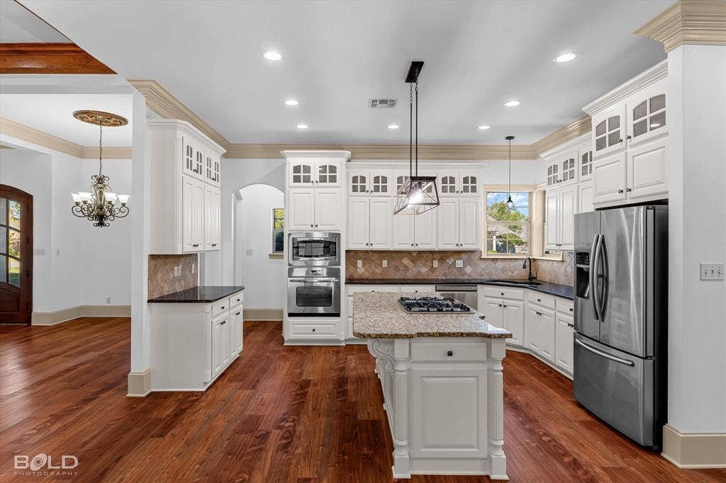 718 Duckwater Landing, Bossier City, LA 71111 Kitchen featuring white cabinetry with glass-front uppers, a central island with a gas cooktop, stainless steel built-in double ovens, stone-finish countertops, and wood-finish flooring