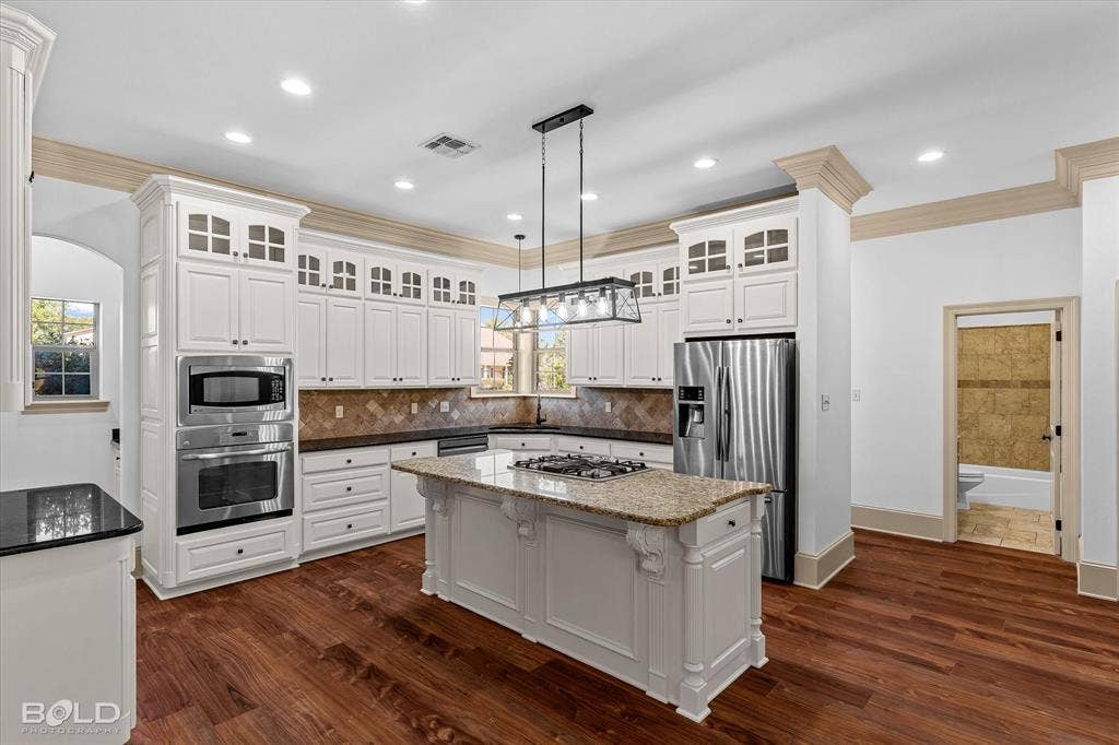 718 Duckwater Landing, Bossier City, LA 71111 Kitchen featuring white cabinetry with glass-front uppers, a central island with an integrated gas cooktop, recessed lighting, wood-finish flooring, and crown molding