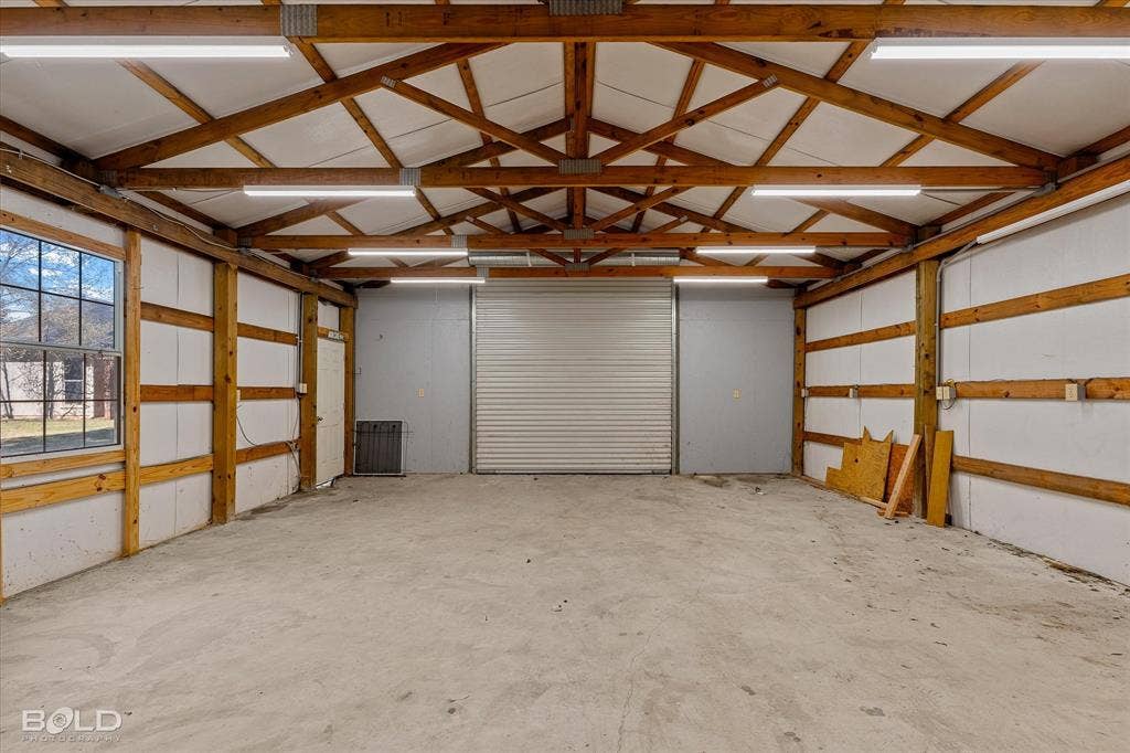 718 Duckwater Landing, Bossier City, LA 71111 Workshop space featuring exposed timber truss framing, concrete flooring, a large overhead roll-up door, linear LED lighting, and natural light via single-hung window