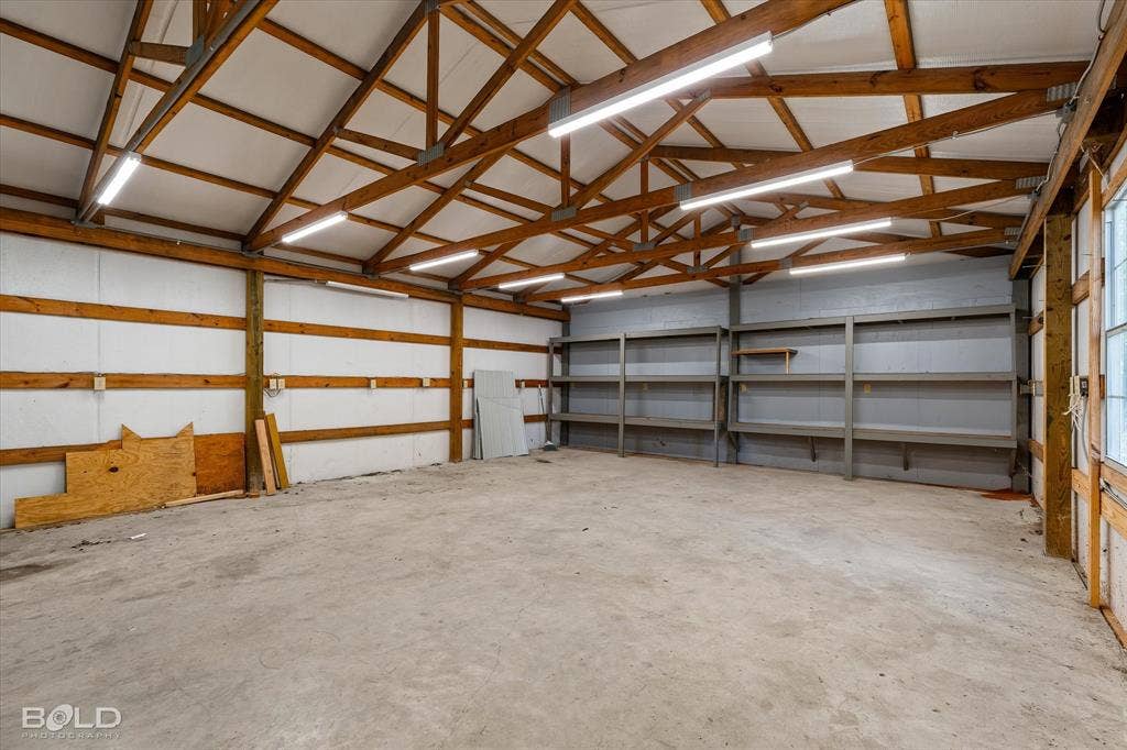 718 Duckwater Landing, Bossier City, LA 71111 Expansive outbuilding featuring exposed wood trusses, concrete flooring, LED overhead lighting, and built-in metal shelving units