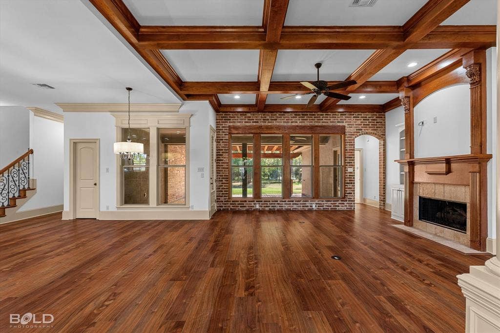 718 Duckwater Landing, Bossier City, LA 71111 Spacious living area featuring coffered wood-beam ceilings, expansive wood-finish flooring, a floor-to-ceiling brick accent wall, and a fireplace with a wood mantel