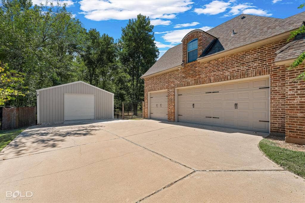 718 Duckwater Landing, Bossier City, LA 71111 Brick exterior residence featuring a three-car garage, an additional detached single-bay storage structure, and an expansive concrete driveway