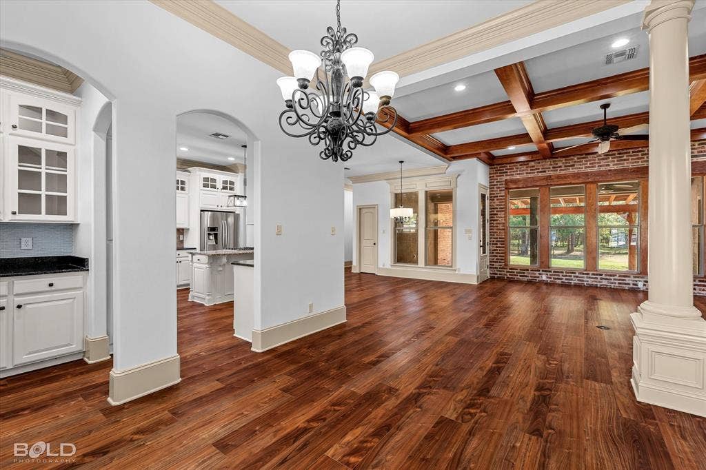 718 Duckwater Landing, Bossier City, LA 71111 Wood-finish flooring, coffered ceilings with exposed wooden beams, interior brick accent wall, ornate metal chandelier, and a prominent decorative column