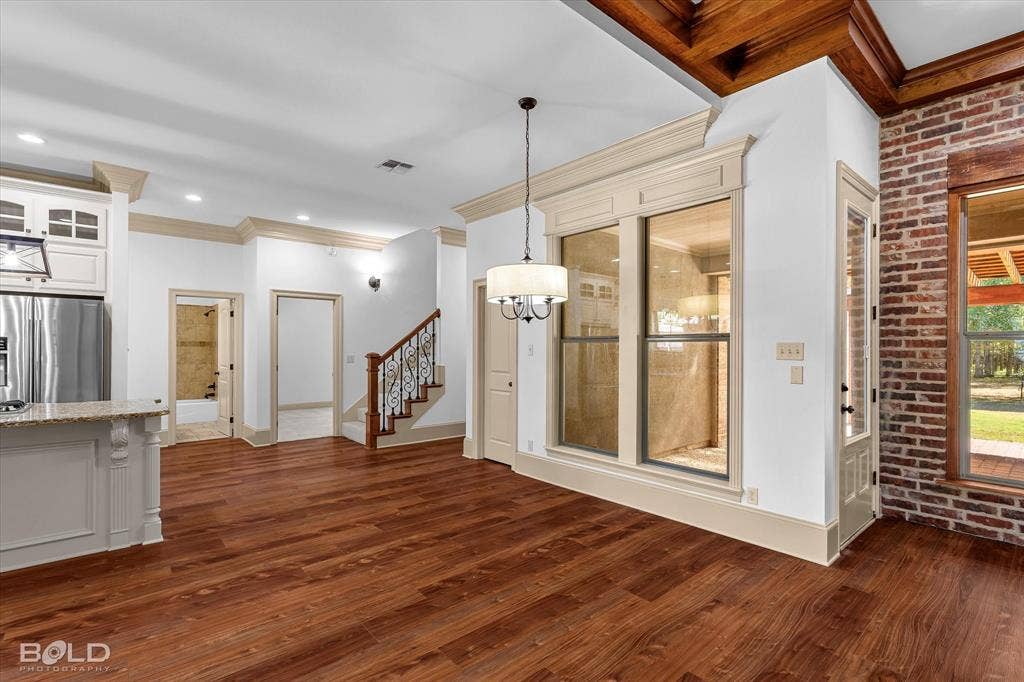 718 Duckwater Landing, Bossier City, LA 71111 Open concept interior featuring wood-finish flooring, exposed brick masonry, coffered wood ceiling details, and a wrought-iron staircase railing