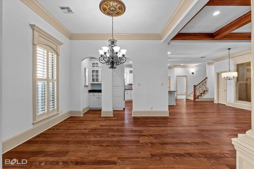 718 Duckwater Landing, Bossier City, LA 71111 Interior featuring wood-finish flooring, recessed ceiling with stained wood beams, decorative ceiling medallion, ornate chandelier, and arched doorway with custom window shutters