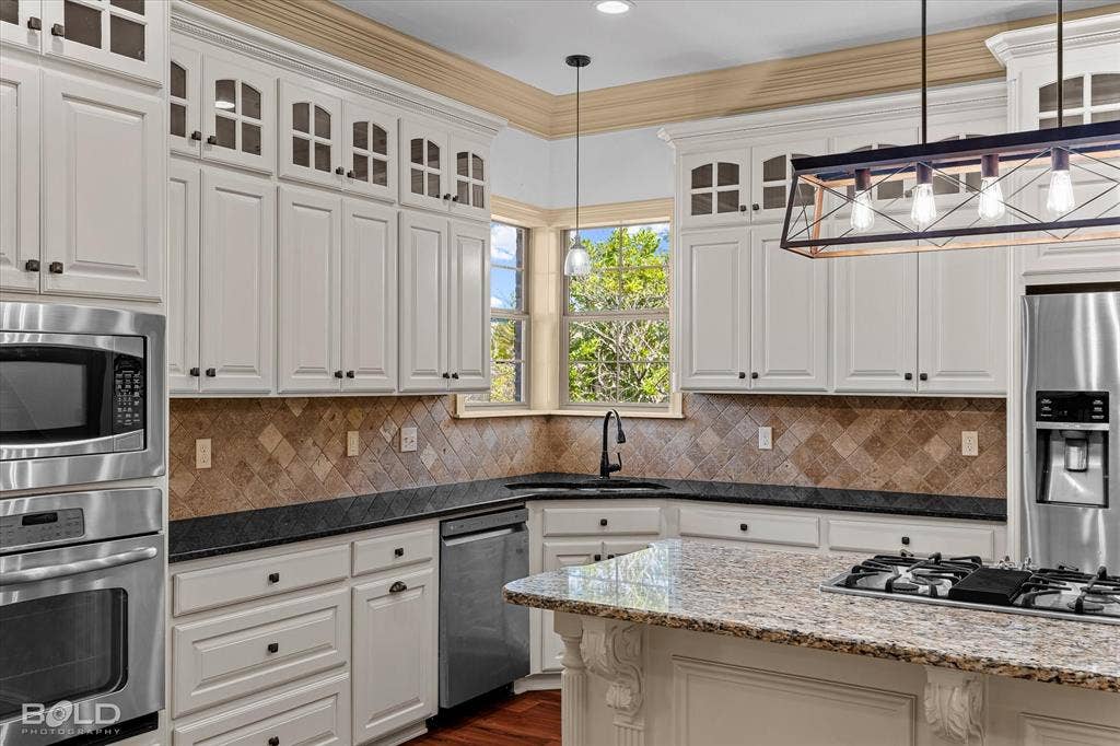718 Duckwater Landing, Bossier City, LA 71111 Kitchen featuring white cabinetry with glass-front uppers, crown molding, stone-tile backsplash, stainless steel appliances, and a central island with a stone countertop