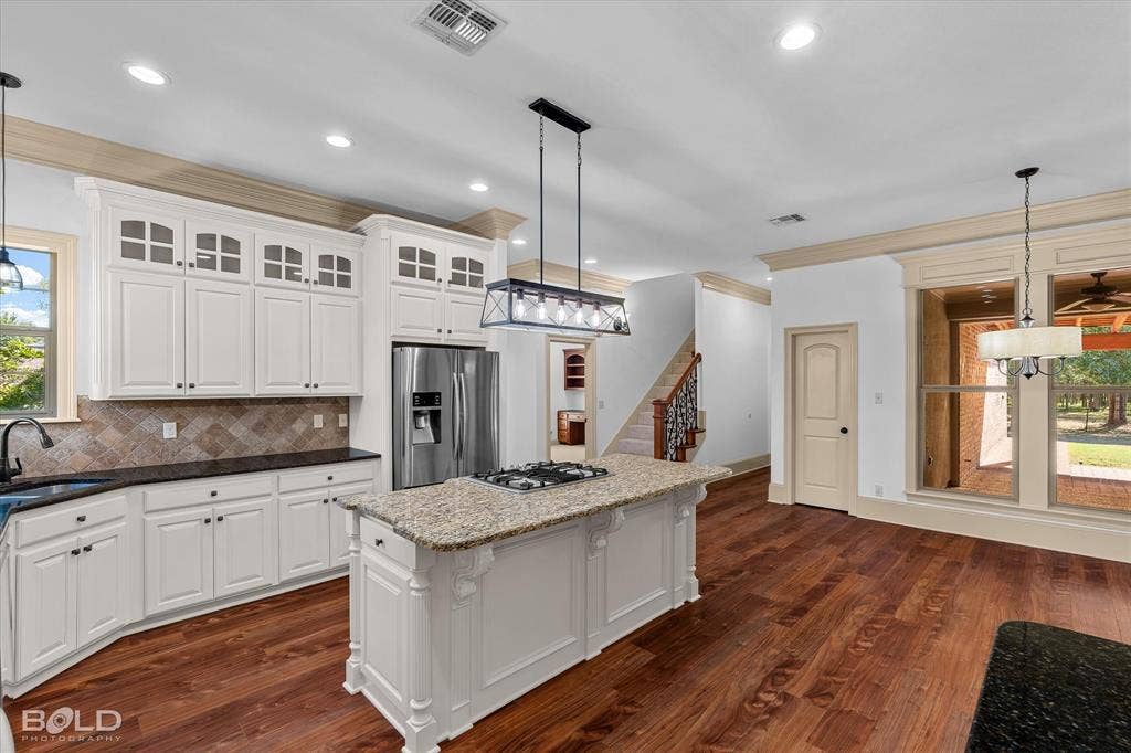 718 Duckwater Landing, Bossier City, LA 71111 Kitchen featuring white cabinetry with glass-panel accents, stone countertops, central island with an integrated gas cooktop, wood-finish flooring, and recessed lighting