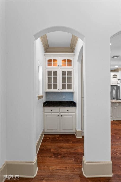 718 Duckwater Landing, Bossier City, LA 71111 Built-in cabinetry with glass-front uppers, stone-surface countertop, tile backsplash, and arched architectural detailing set atop wood-finish flooring