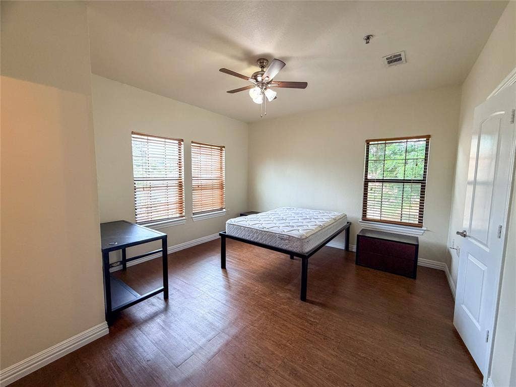 2410 S 2nd Street, #1373, Waco, TX 76706 Bedroom 5: Spacious room featuring wood-finish flooring, two windows with blinds, a ceiling fan with integrated lighting, and a white paneled door