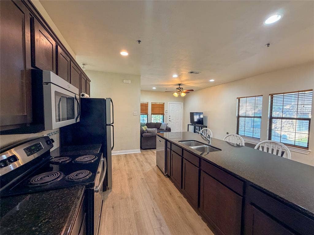 2410 S 2nd Street, #1373, Waco, TX 76706 Kitchen featuring dark wood cabinetry, stainless steel appliances, dark countertops, and wood-finish flooring
