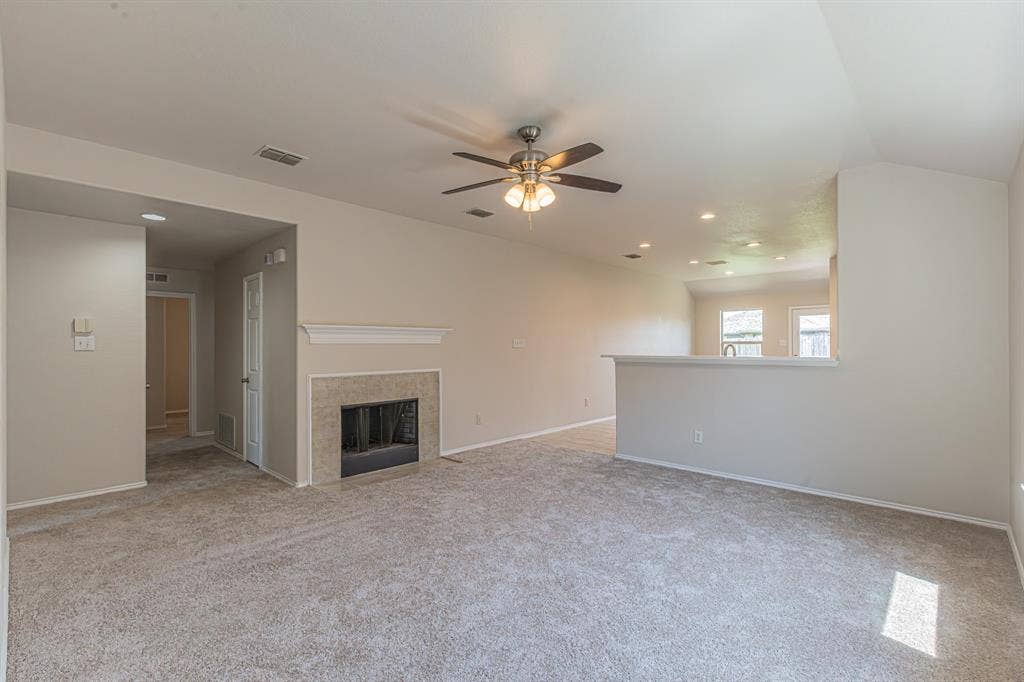Spacious living area featuring neutral carpeting, a tiled fireplace with a mantel, and a ceiling fan